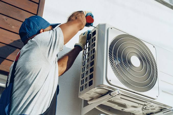 A technician using gauges to check an air conditioning unit outdoors